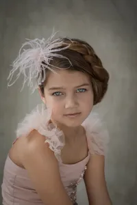 Girl's close-up studio portrait with a braided crown hairstyle and feather headpiece