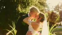 Wedding videography still of couple holding each other outdoors surrounded by greenery and plants
