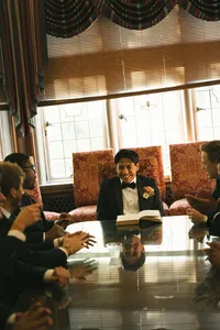 groom at formal indoor seating - Photograph of groom in formal black tuxedo seated in elegant room with patterned armchairs and large windows
