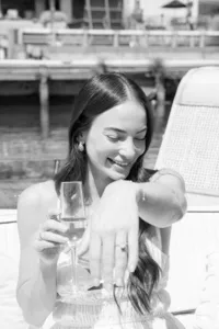 Woman sipping champagne and showing off her ring during an engagement session, photographed in black and white
