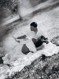 Black and white Michigan maternity photos of a couple lying on a white blanket in a grass field.