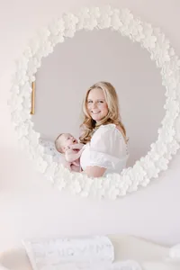 Mother smiling while holding her newborn, framed by a round floral mirror