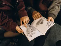 Close up of a couple pointing to illustrations in a book, by Michigan engagement photographer Grace Wan.