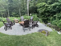 Outdoor fire pit and Adirondack chairs surrounded by woods at Brookside Retreat
