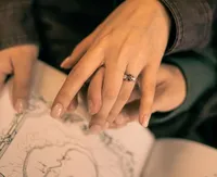 Close up of a woman's engagement ring on her hand as she and her fiancé point at an illustration in a book.