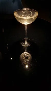 alcoholic drink reflecting on a dark shiny surface, light in color in a martini like glass