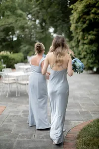 Bridesmaids in dusty blue satin gowns walk together carrying hydrangea bouquets