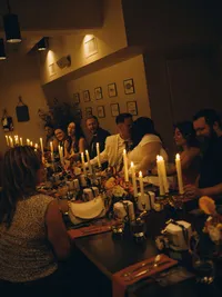 A bride a groom kiss as they sit at a long table, decorated with candles, with their family.