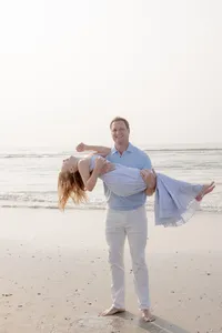 Father carrying his laughing wife during a sunset beach portrait session