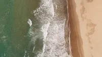 aerial beach coastline with waves - Wedding videography still overhead view of ocean waves meeting sandy beach with coastal landscape