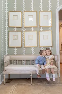 Siblings sitting on a bench in front of a framed gallery wal