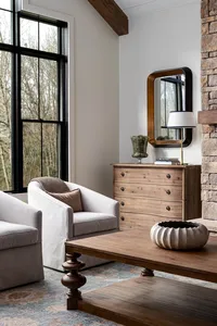 Cottage living room interior design, with oak dresser, black windows, matching chairs, and a rock fireplace.