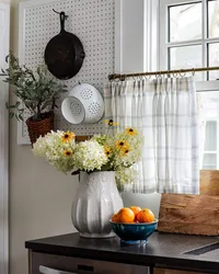 Kitchen decor details, fresh wildflowers, and tangerines in a bowl in front of a plaid cafe curtain.