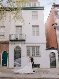 Bride and groom walk past a historic Philadelphia rowhouse with a flowing veil trailing behind