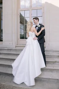 Bride and groom share a smiling embrace on stone steps, her satin bow dress detail visible