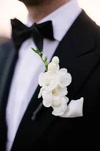 Close-up of a white freesia boutonniere pinned to the groom's black tuxedo lapel