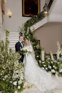 Bride and groom pose on an indoor staircase dressed with a cascading white and green floral garland