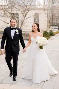 Bride and groom walk hand in hand outside the Philadelphia Museum of Art on a bare winter tree lined path