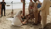 bride washing groom's feet during beach ceremony - Wedding videography still of bride washing groom's feet during ceremonial moment on sandy beach