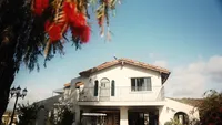 Wedding videography still of residential venue building with bright blue sky and flowering plants