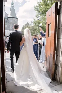Bride and groom walk out through open church doors as guests cheer and wave ribbon wands
