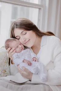 Mother holding her newborn cheek to cheek with eyes closed