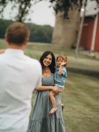 A mother holds her toddler as their husband/father looks at them with his back to the camera.