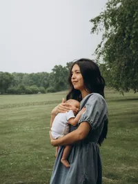 Motherhood portrait of a mom holding her newborn baby while looking off into the distance.