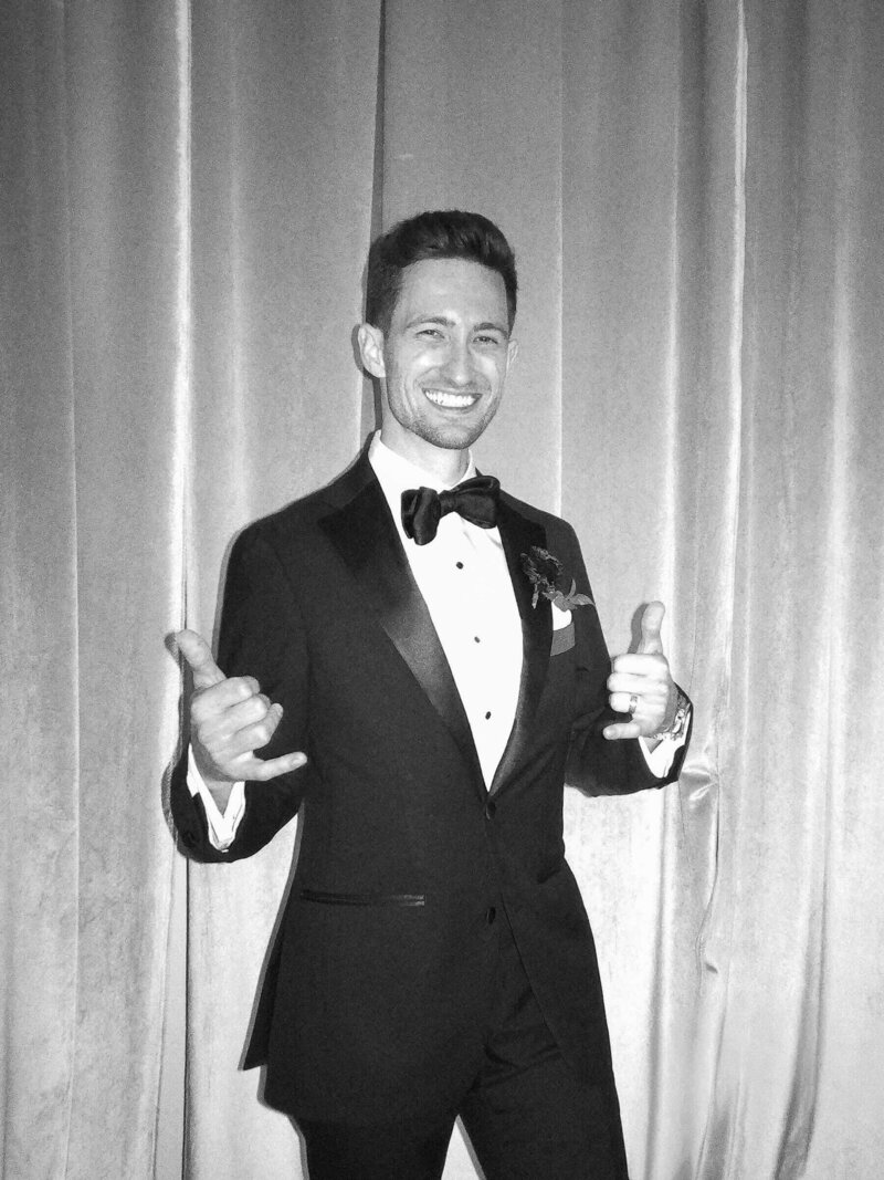 Wedding guest in a tuxedo making a playful gesture for a black-and-white photo