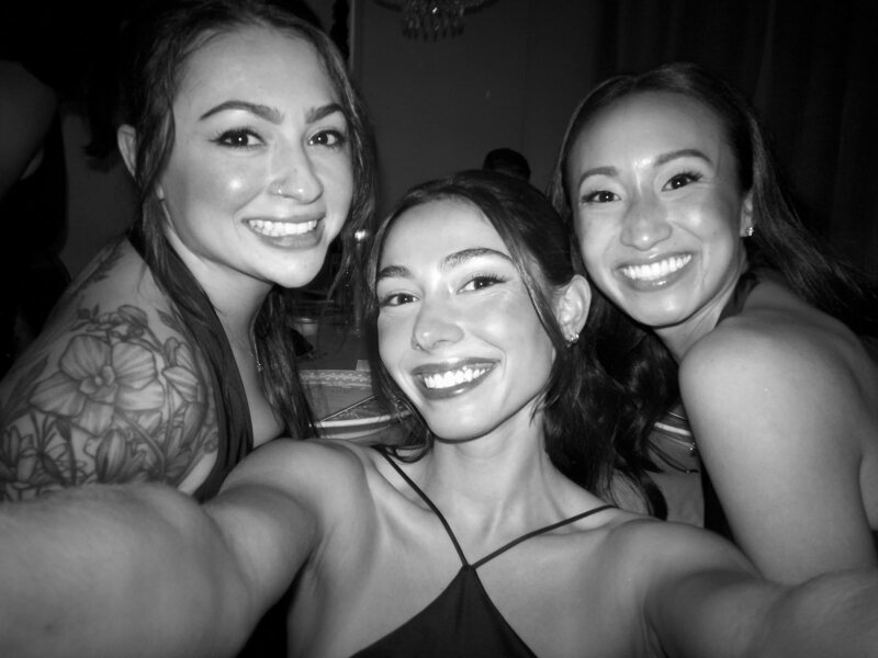 Three friends smiling for a black-and-white wedding selfie