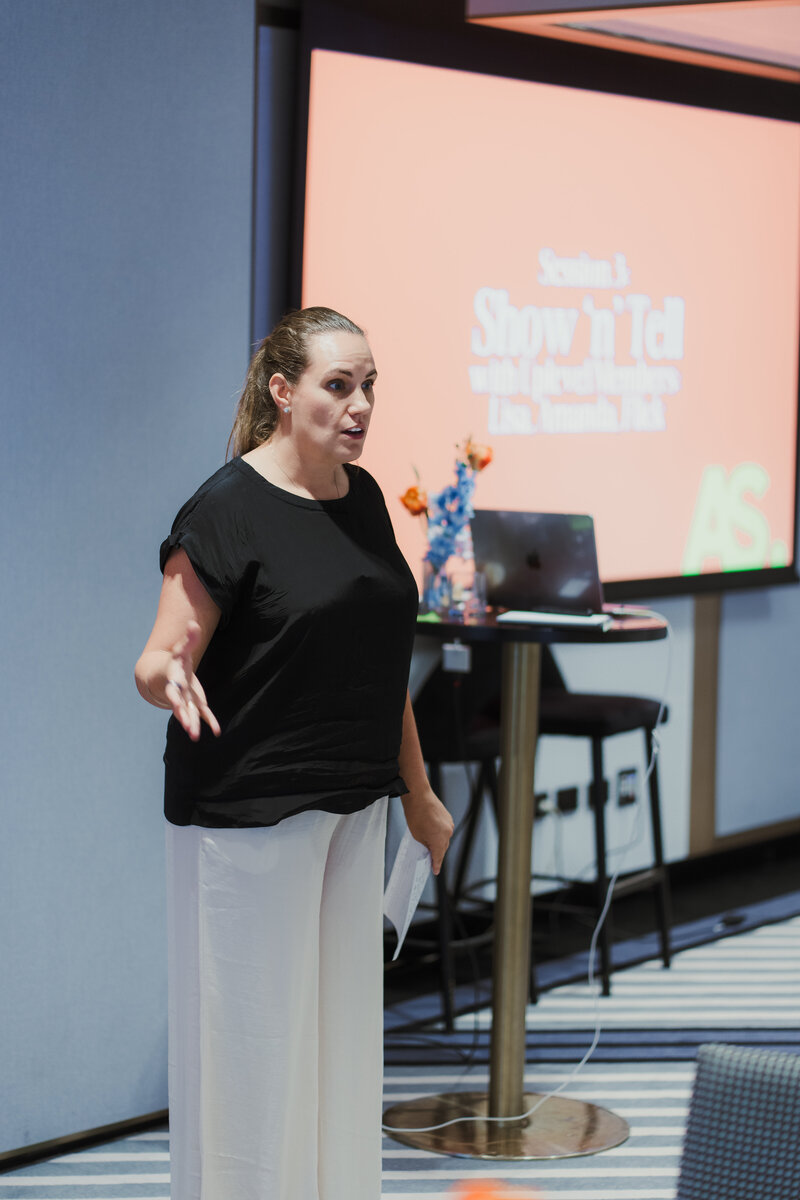 Flick Browne presenting at an Uplevel members session, mid-explanation beside a laptop and a slide