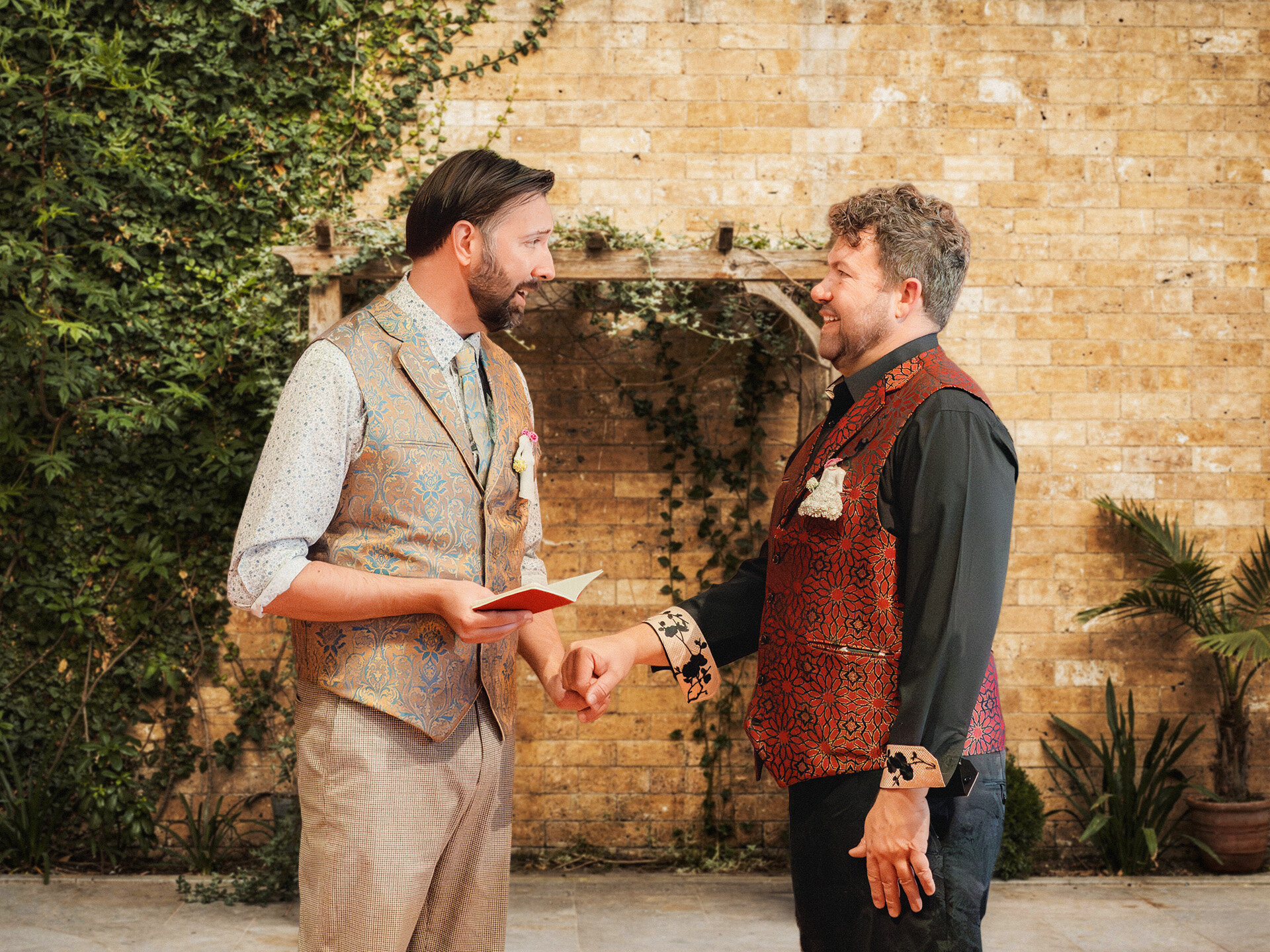 Two grooms holding hands and exchanging vows during an intimate bohemian ceremony