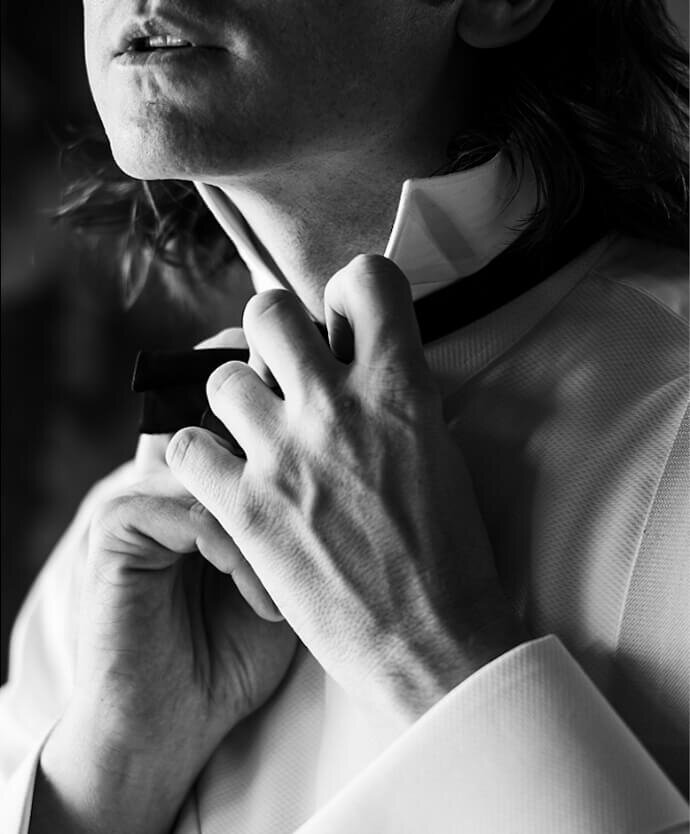 Groom adjusting his bow tie in a black-and-white portrait