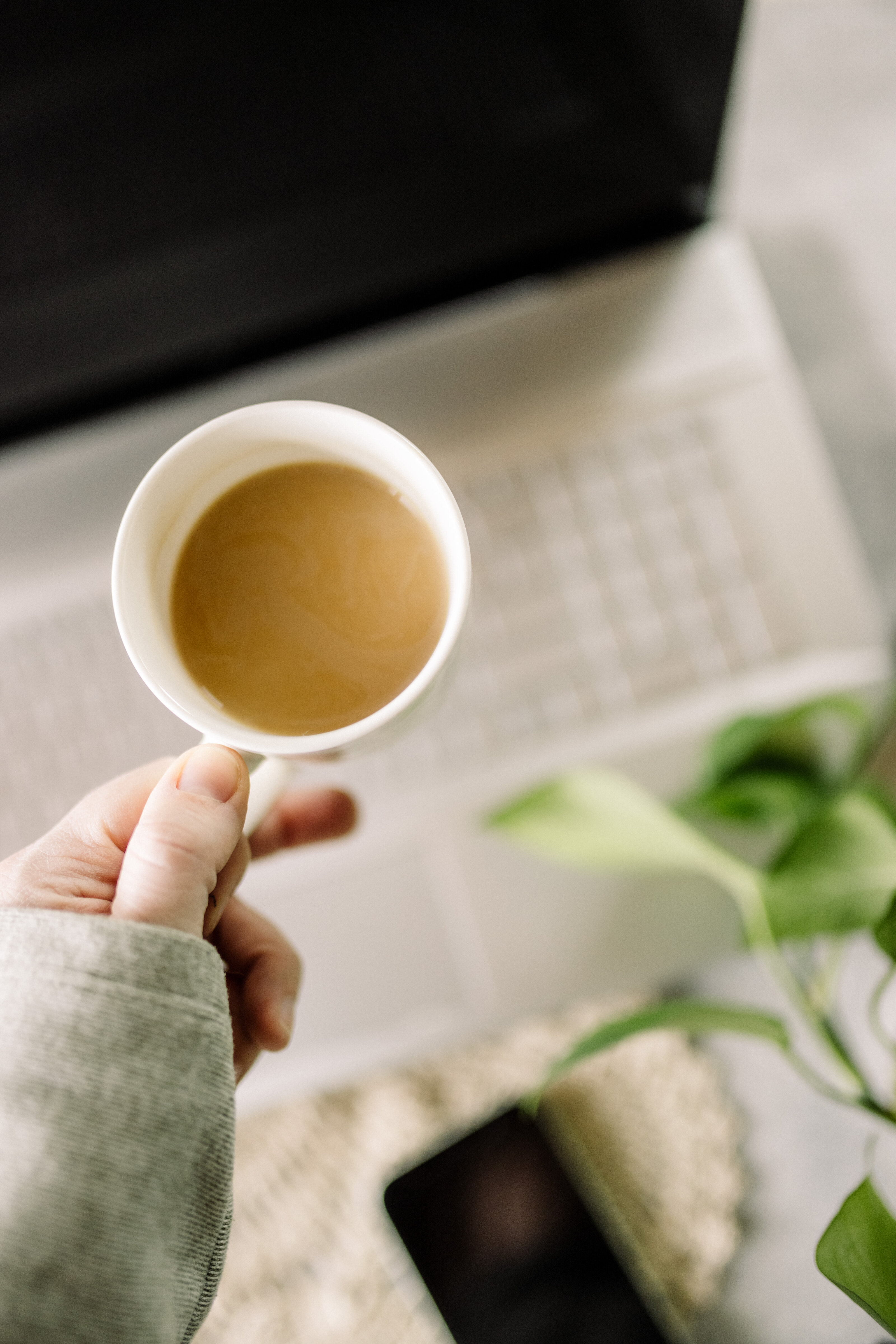 Hand holding a cup of coffee over a laptop