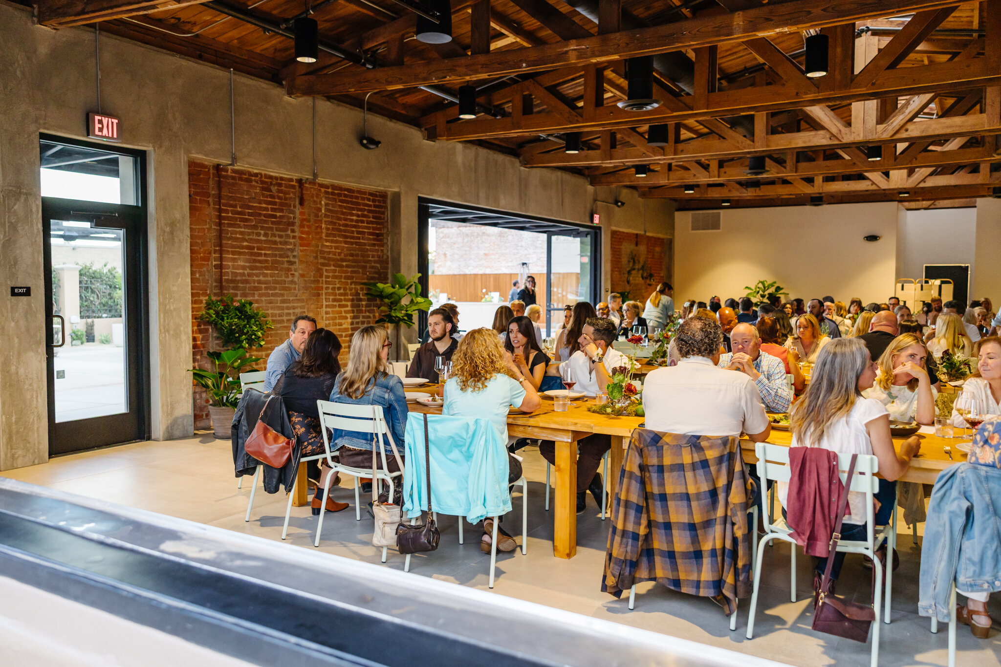 Guests dining at long wood tables inside Palomino with the patio visible through open doors.