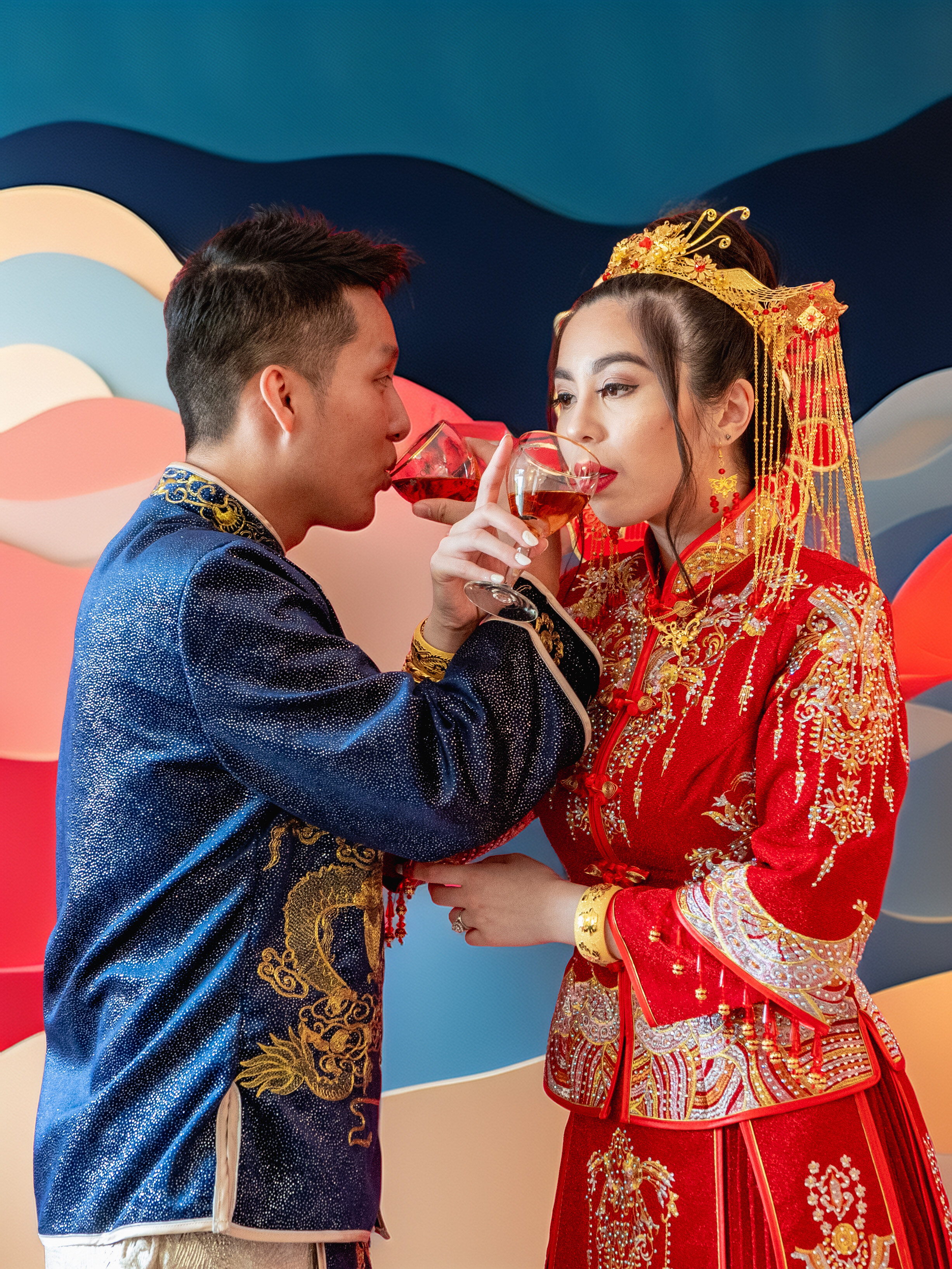 Chinese wedding couple sharing a traditional cross-cup toast against a colorful sculptural wall