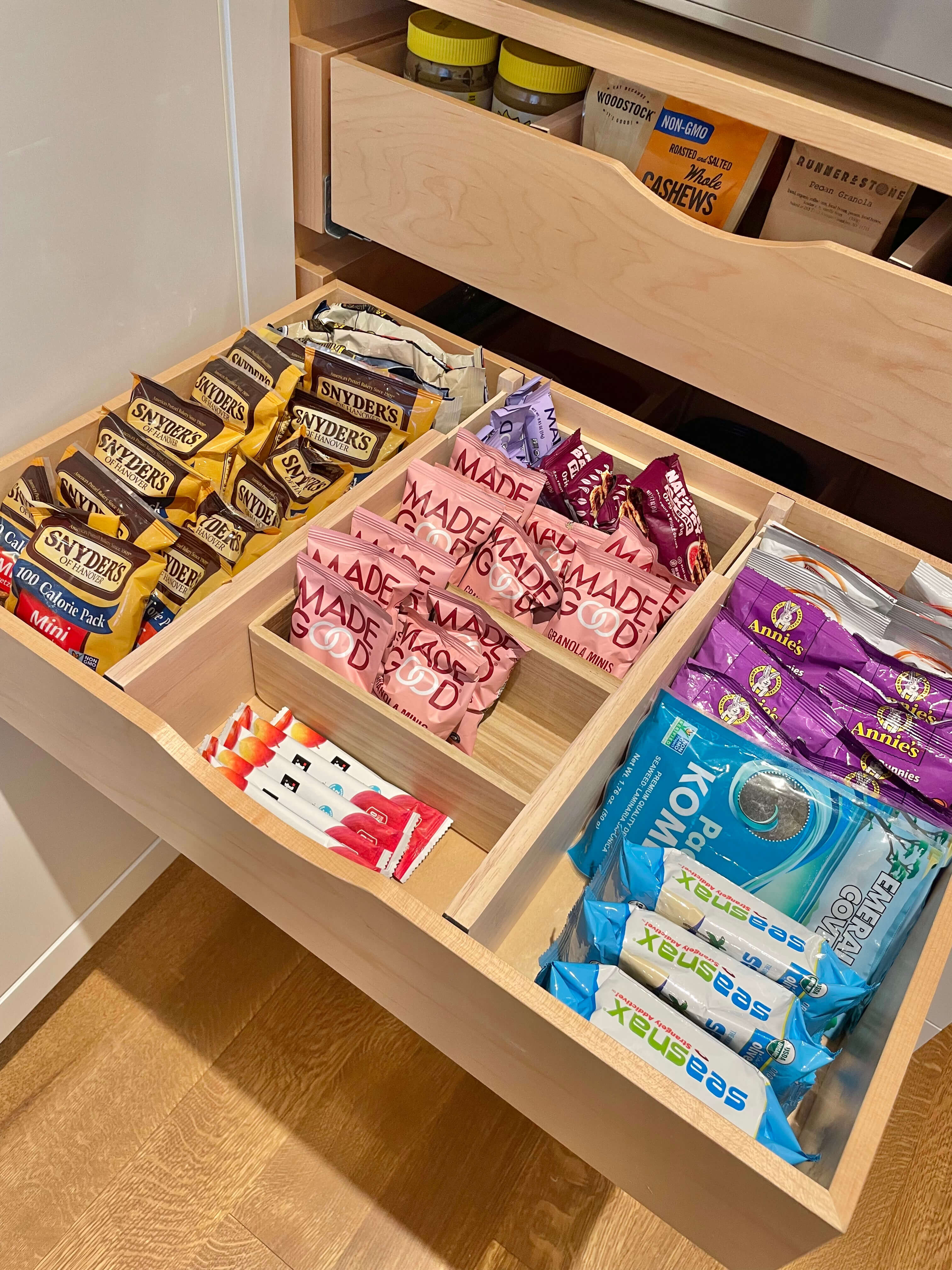 Organized kitchen snack drawer with wooden dividers separating chips, granola bars, and packaged snacks.