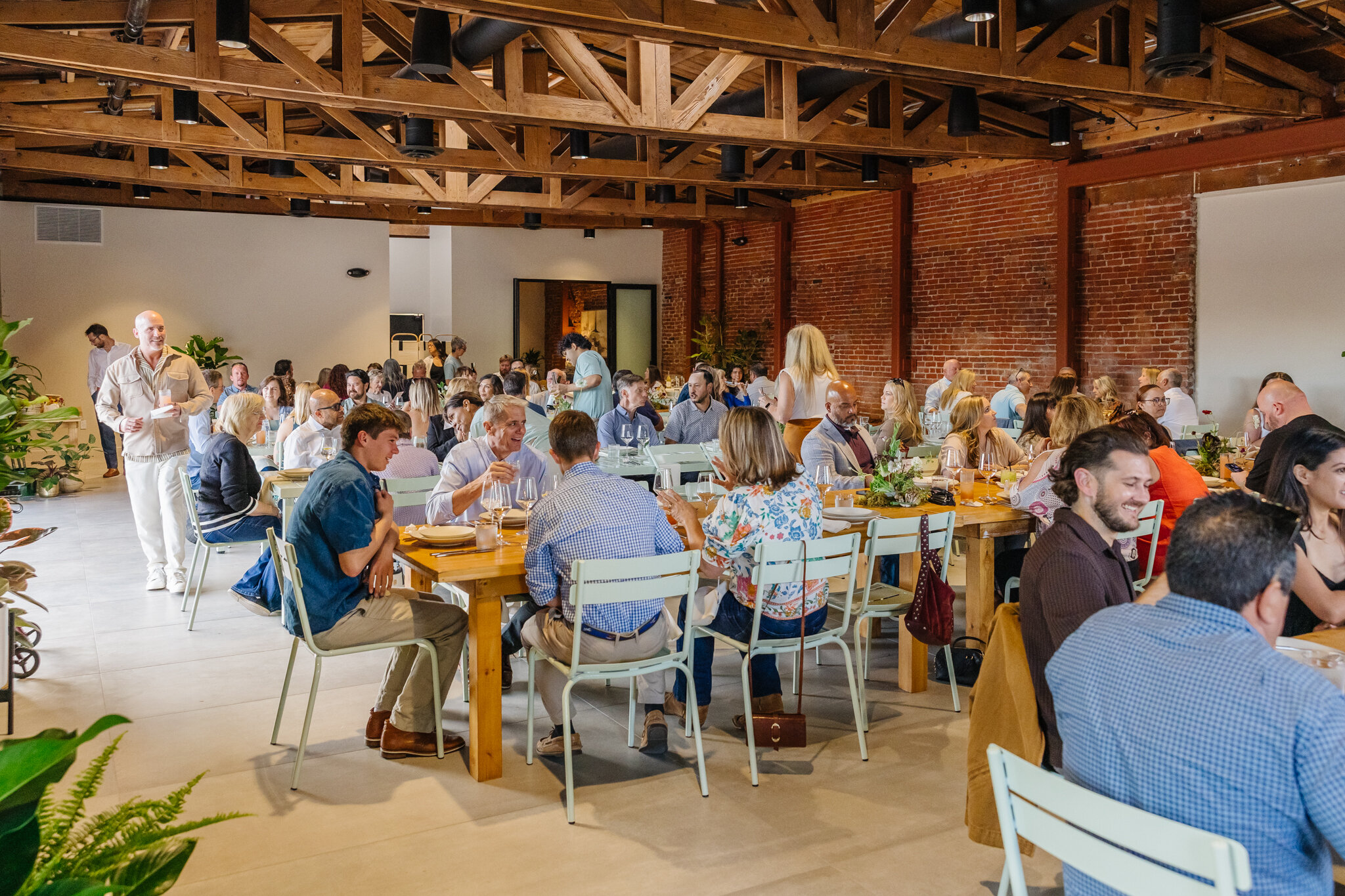Guests sharing a lively seated dinner at long wood tables inside Palomino’s indoor event space.