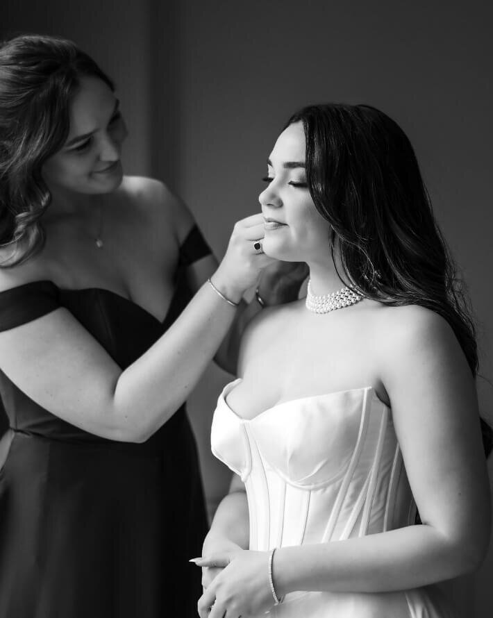 Bridesmaid applying lipstick to the bride in black and white