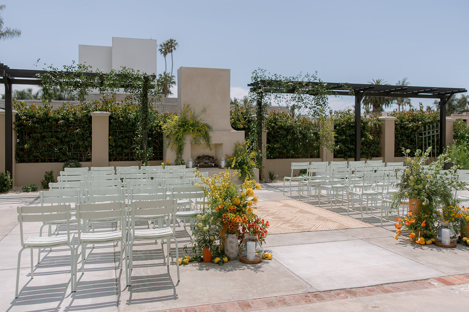 Rows of Coastal Sage chairs facing the outdoor fireplace with seasonal floral arrangements on Palomino’s patio.