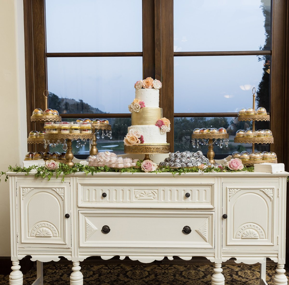 Wedding dessert and cake display with florals, pastries, and gold serving pieces.