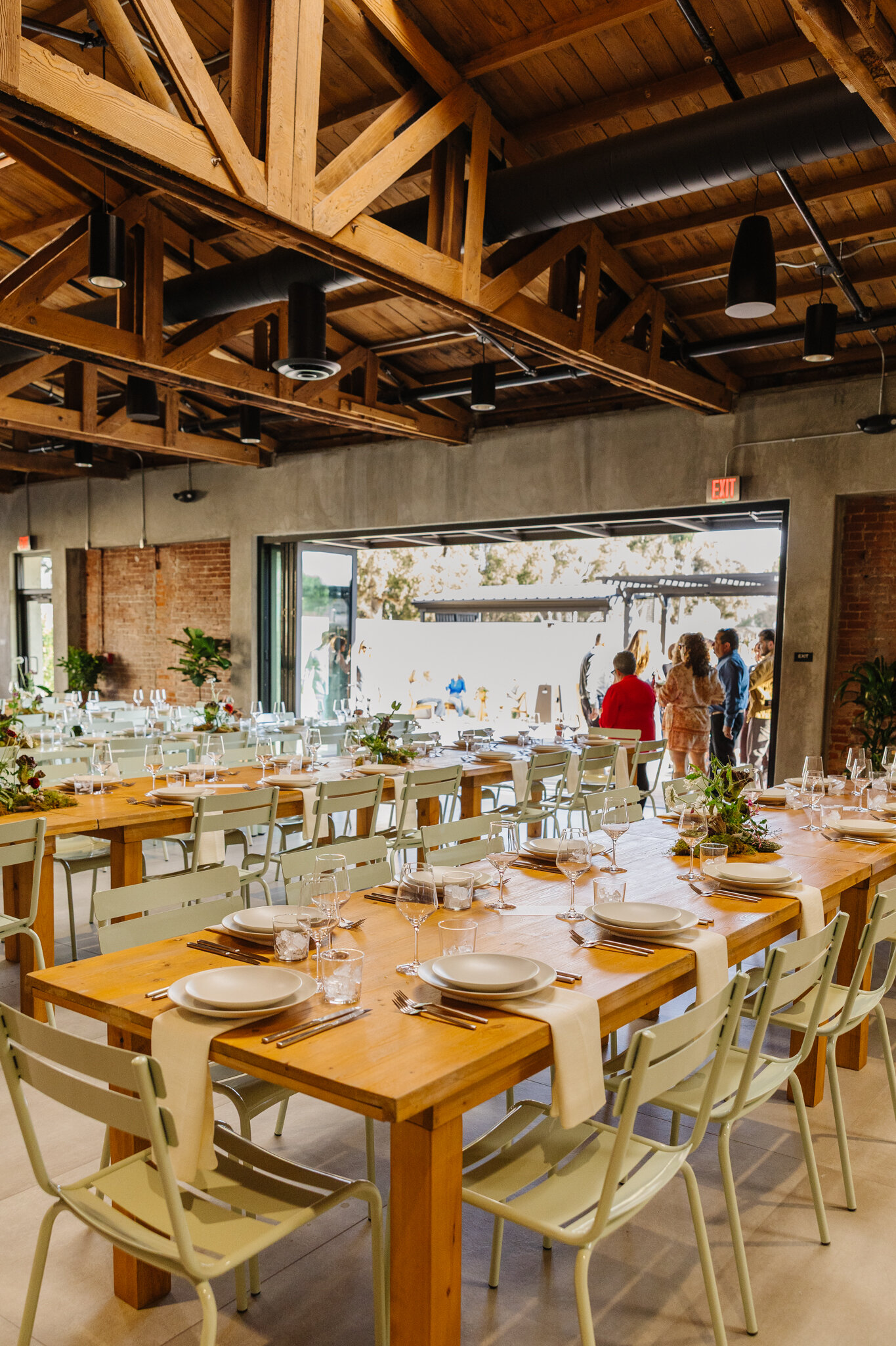 Long dining tables set with white plates and glassware beside Palomino’s open connection to the patio.