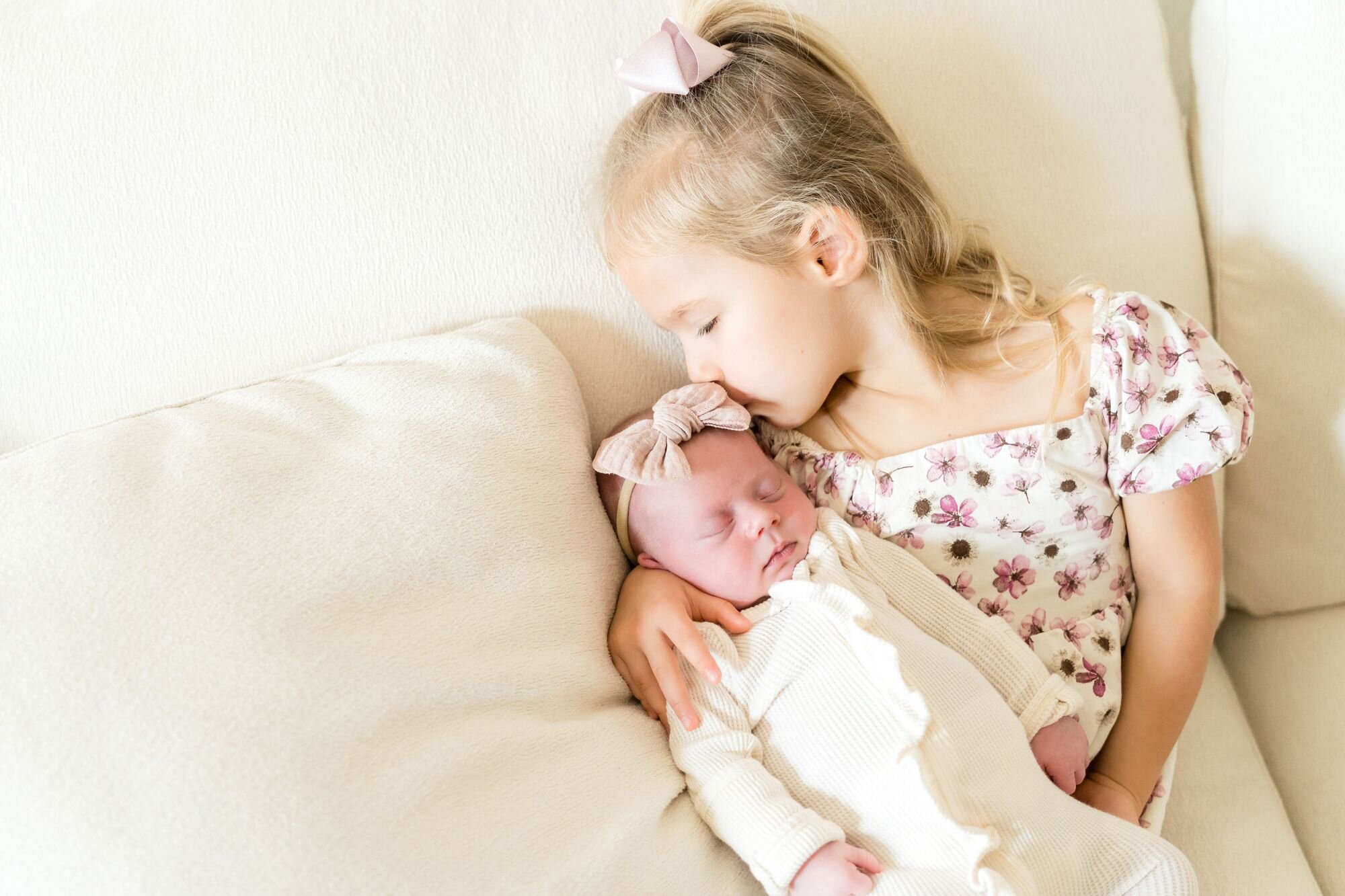 Big sister kissing her sleeping newborn sibling on the couch