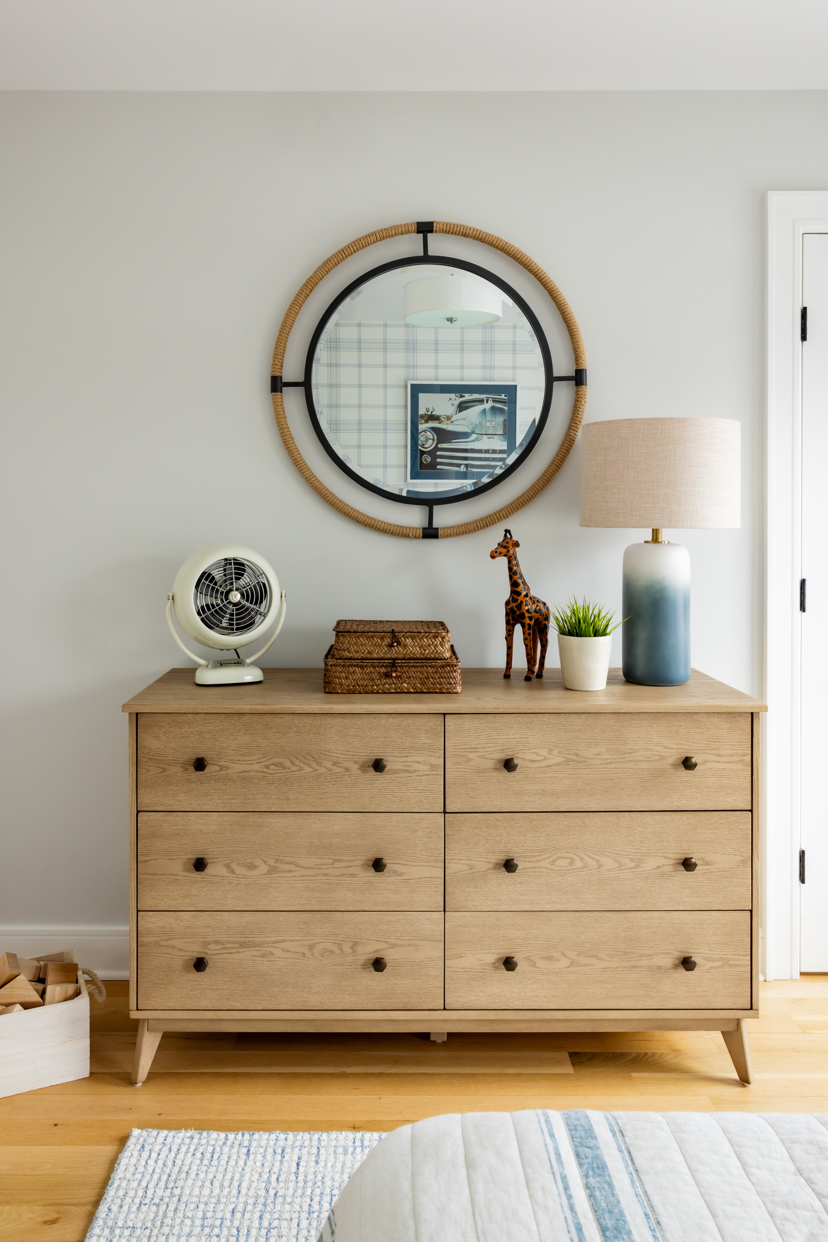 Light wood dresser styled with a round rope mirror, a ceramic table lamp, a woven box, and a small potted plant