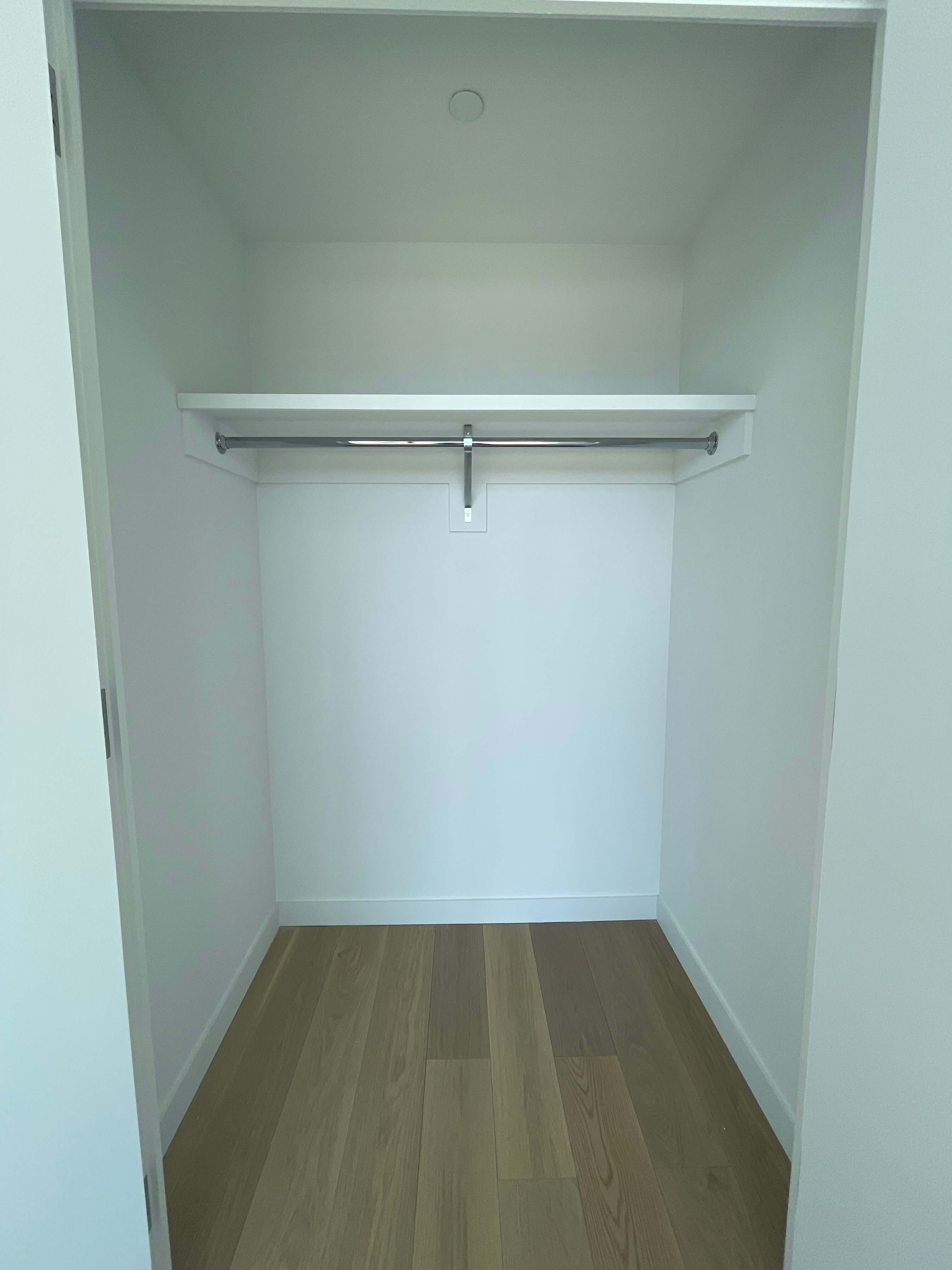 Empty bedroom closet with a single hanging rod and shelf before custom organization.