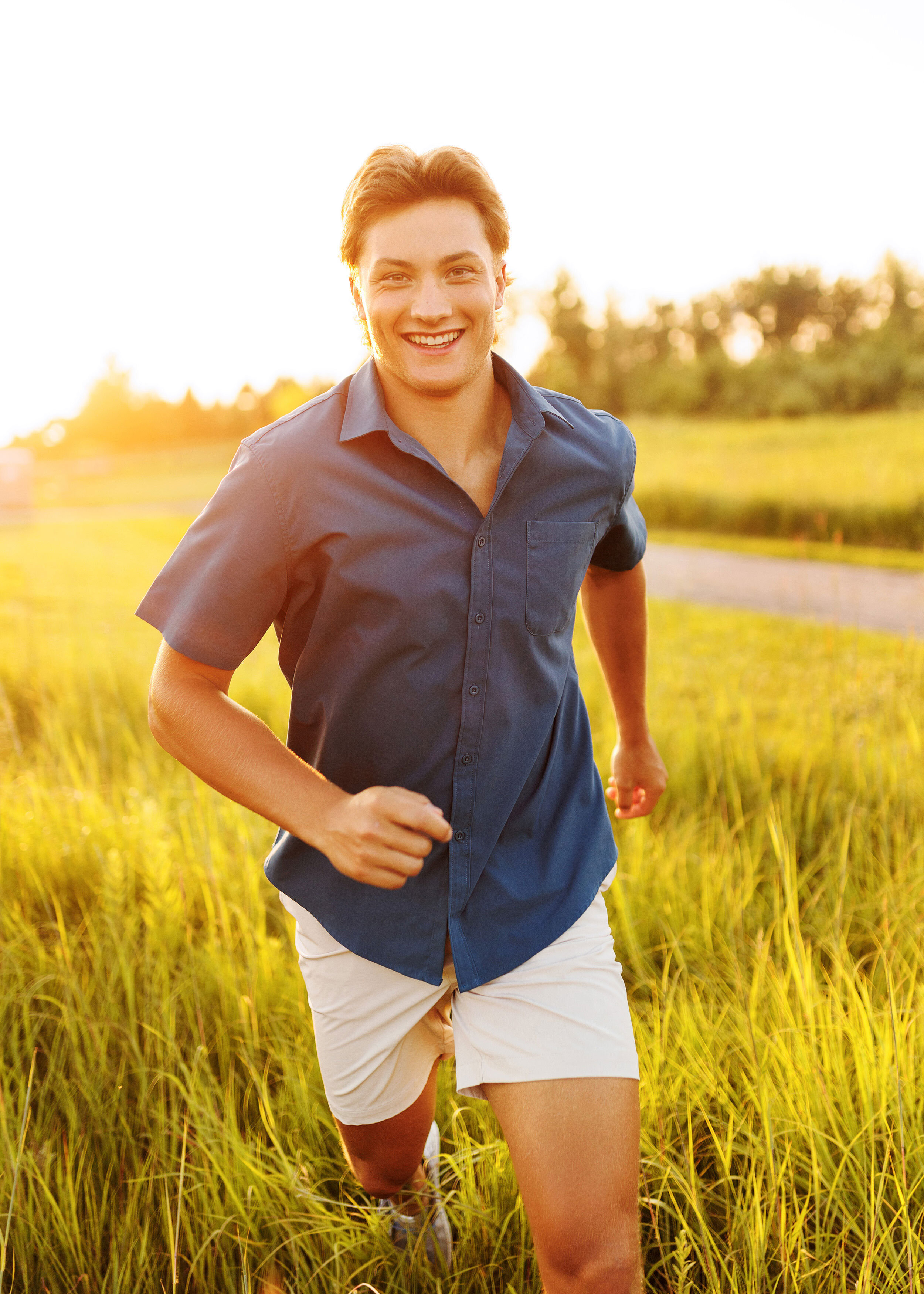 high school senior guy running through sun drenched field during his outdoor golden hour senior photos