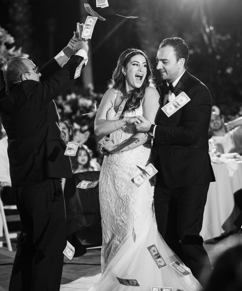 Newlyweds smiling during a lively wedding money dance in black and white