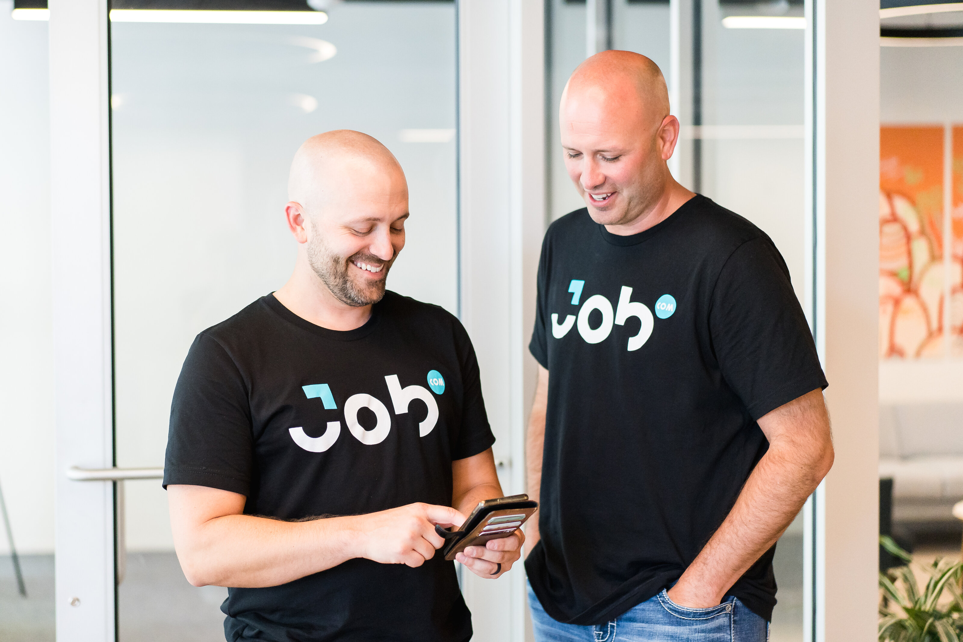 Two Job.com coworkers laughing over a phone in the office