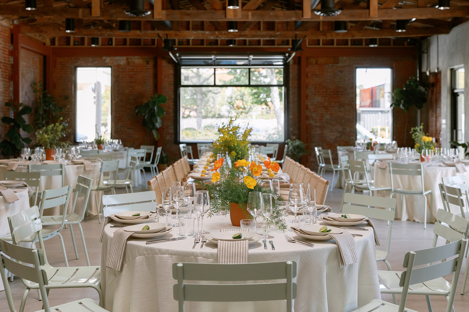 Round and rectangular reception tables with white linens, Coastal Sage chairs and orange floral arrangements inside Palomino.