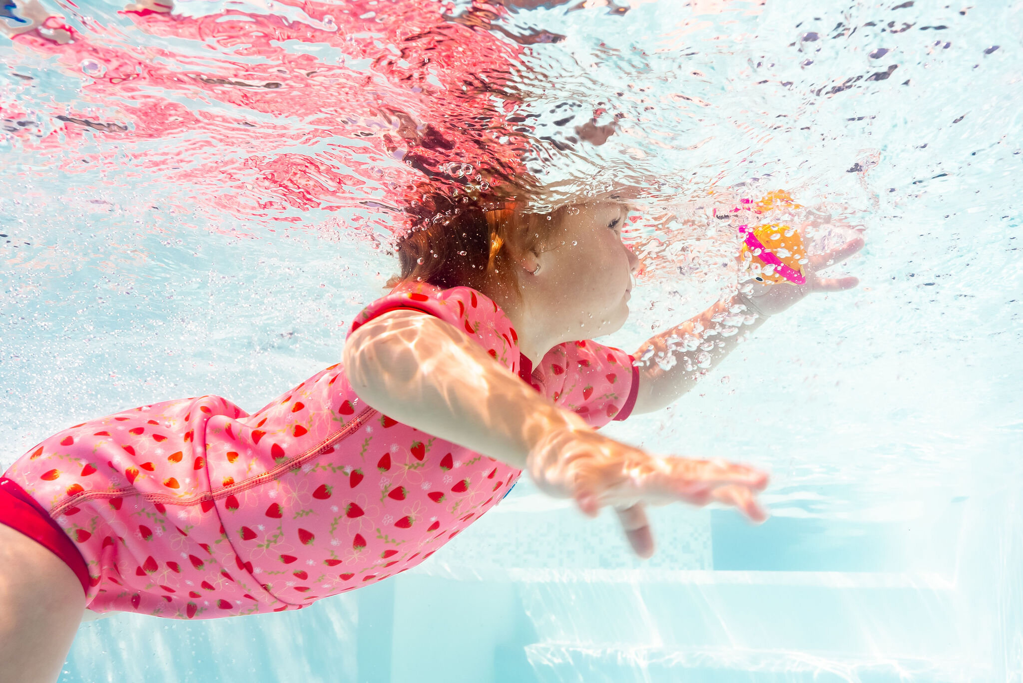 Underwater photography of a girl jumping in a strawberry print swimsuit for Splash About